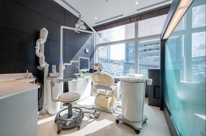 A dental treatment room with a modern chair, overhead light and floor-to-ceiling windows